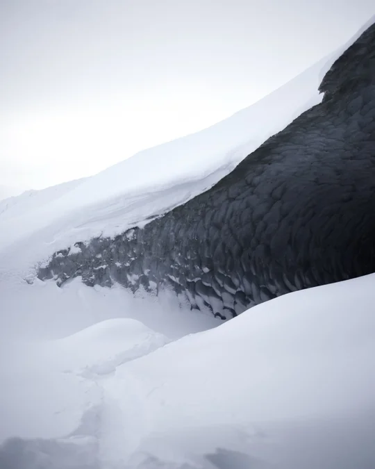 Snow curves toward a dark opening beneath the glacier