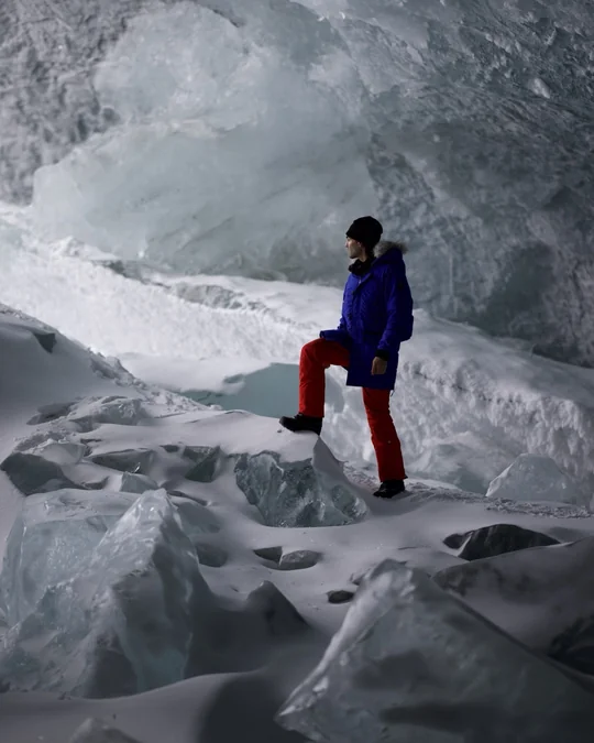 A hiker in red trousers stands inside a blue ice chamber