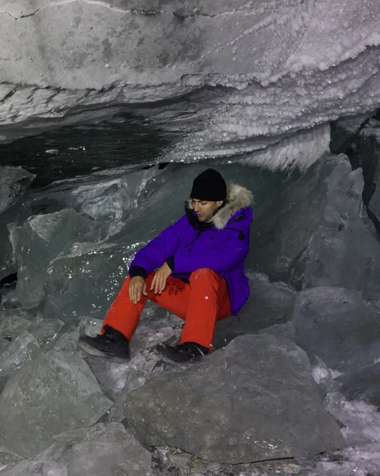 A seated hiker rests beneath a low ice ceiling